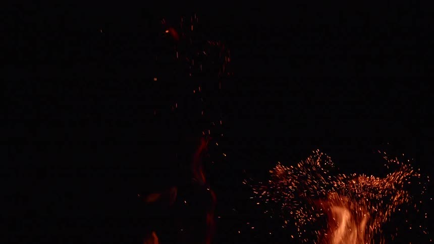 The tops of flames send sparks into a pitch black sky