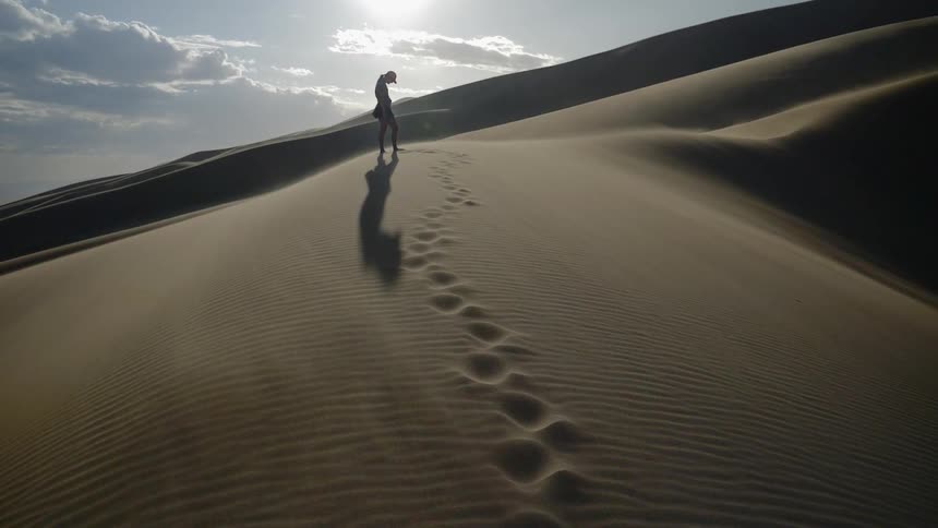 The silhouette of a person standing with head bowed on a sand dune