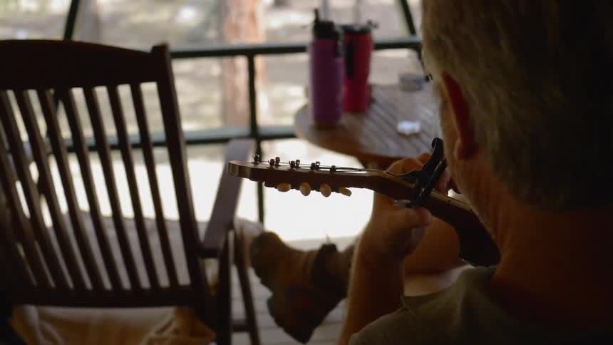 A man plays a stringed instrument while sitting outside on a patio