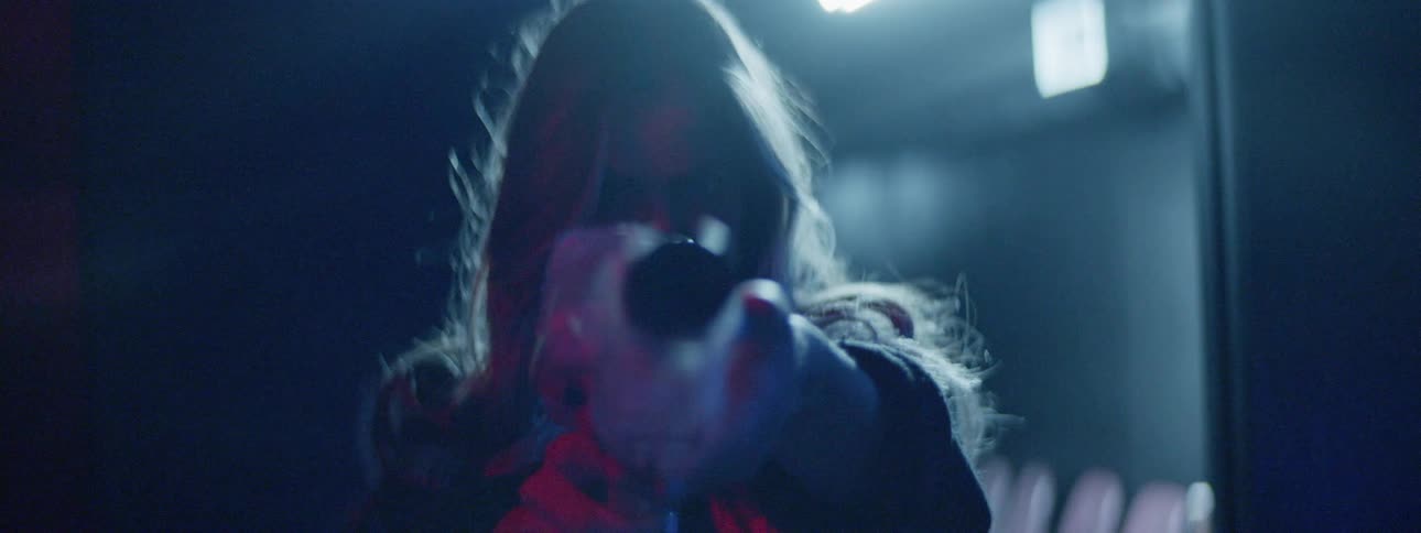 A woman points something at the camera while green lights flash around her neck