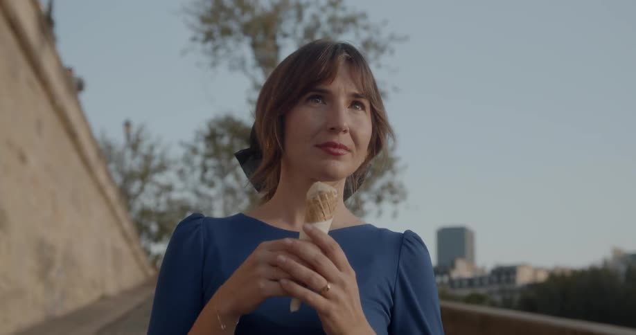 A beautiful woman eating ice cream while walking on the park