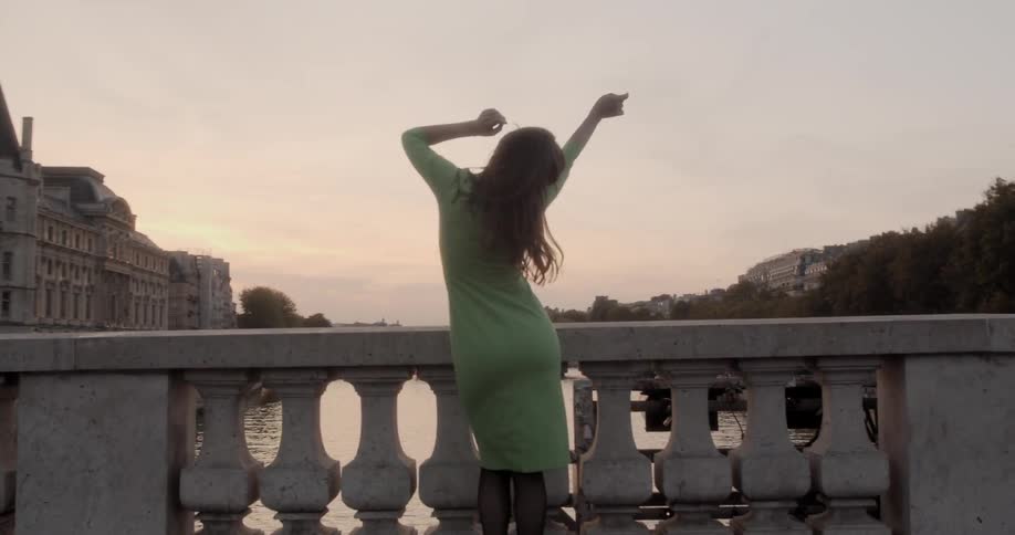 Woman dance on stone bridge overlooking river with palace in background