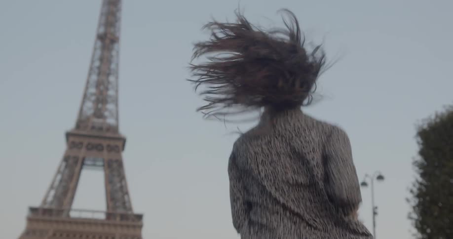 A woman in a leopard print dress smiles an laughs as she runs towards the eiffel tower while looking over her shoulder is if shes being pursued