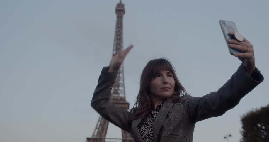 Woman poses and takes a selfie with a smartphone in front of the eiffel tower