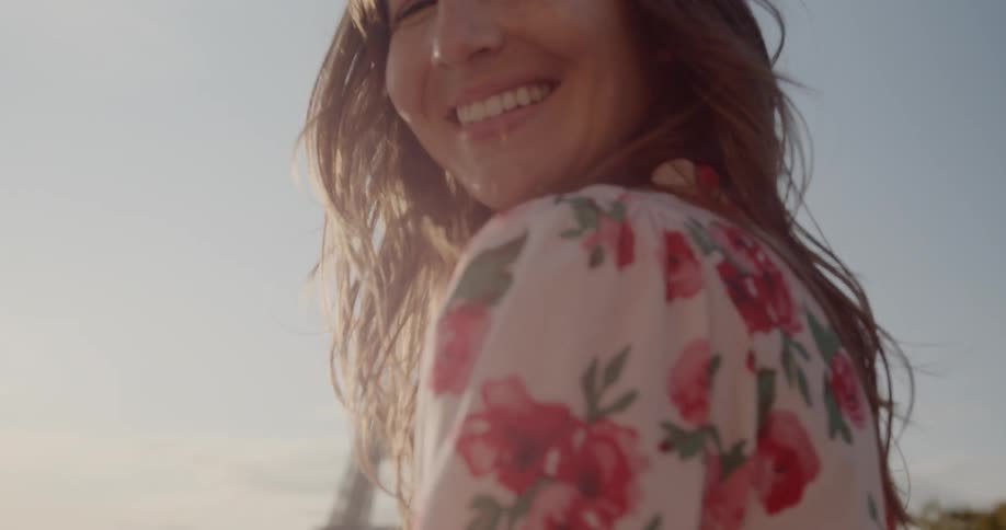 Woman smiles as she looks over her left shoulder while near the eiffel tower