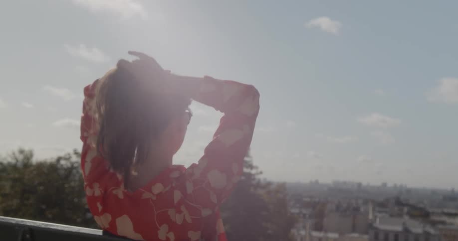 Woman combs her hair into pony tail while overlooking city