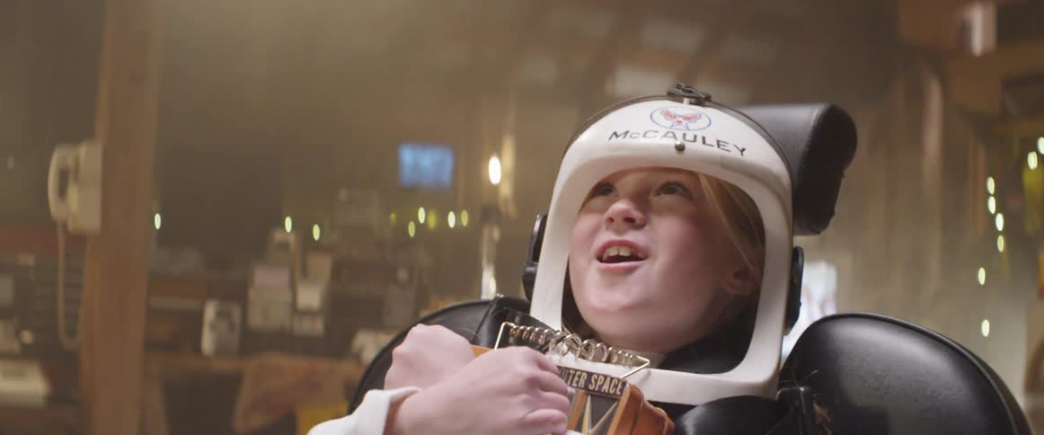 A young girl wearing an astronaut costume picks up a lunch box