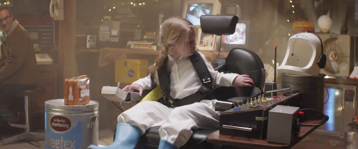 Child dressed in space costume sits in reclining seat and straps herself in