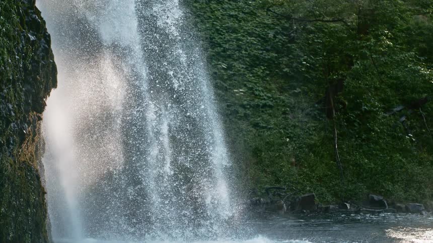 A waterfall flows over a rocky face into a river below