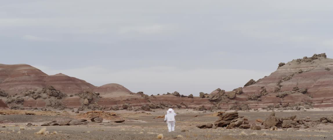 Person dressed in all white walks towards some mountains in a desert
