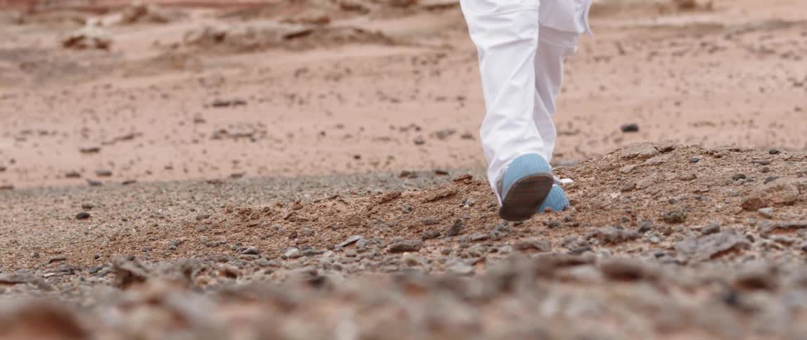 A young person in white pants jogs across the rocky dirt