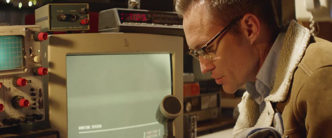 A man talks in to a microphone while a screen flashes in front of him