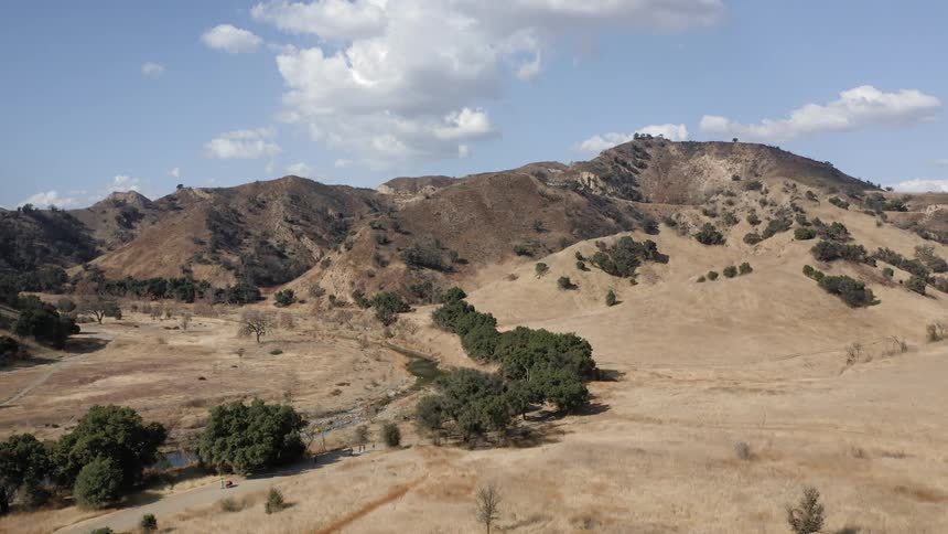 Hills loom over a valley with a creek running through it under a partially cloudy sky