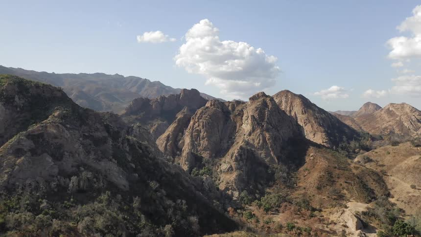 A desert mountain range with sporadic trees and brush