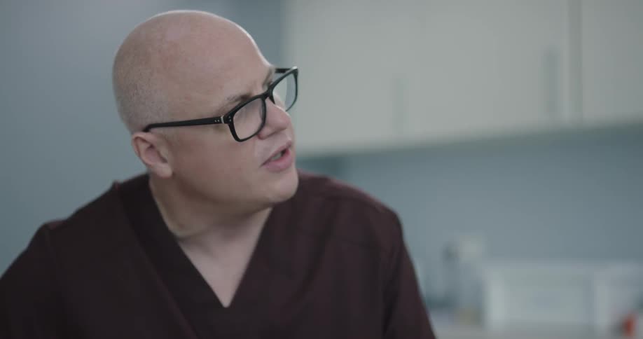 A bald male nurse in eyeglasses pointing at a medical display
