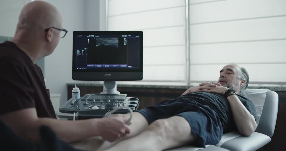 Man lying on a table while a bald man in scrubs takes an ultrasound of his knee