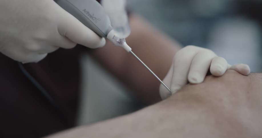 Two people give another person an injection while watching on a screen