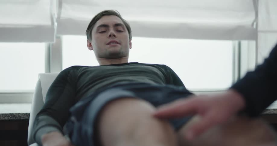 A doctor inspects a patients knee and flexibility while the patient cringes on the bed