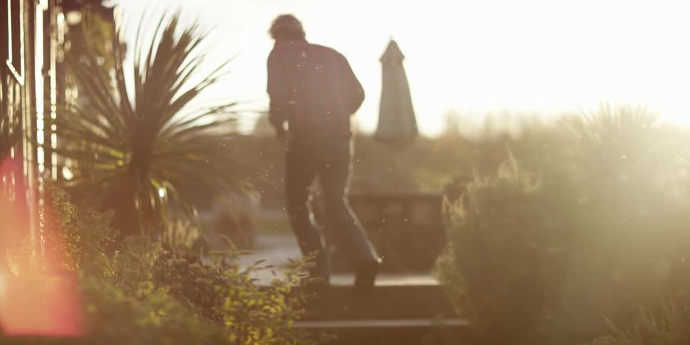 An older man walks up some stairs in a garden