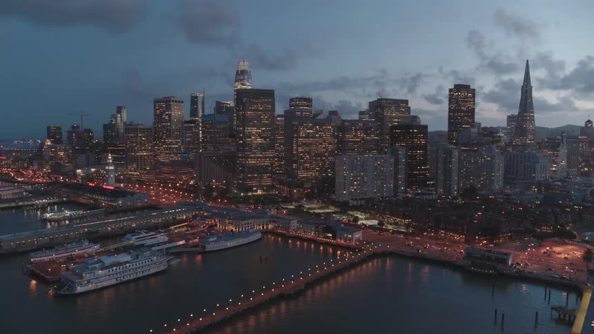 Skyline of the illuminated city with tall buildings and skyscrapers next to the sea at dusk