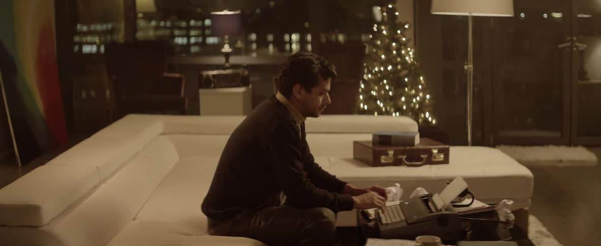 A man is sitting on a couch using a typewriter