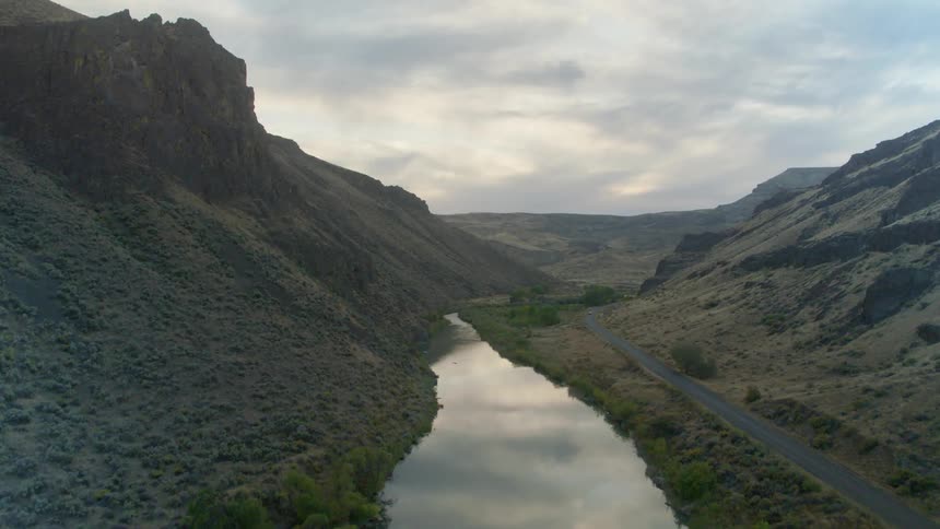 A road next to a river between two mountains with the sky in the background