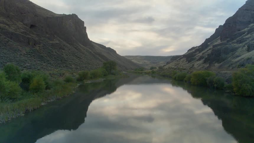 River cuts between two mountains and reflect the cloudy sky