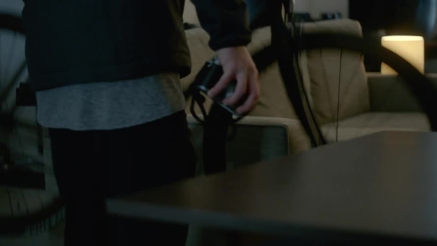 A man picks up a camera and a bike indoors