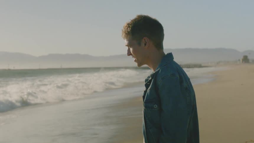 A man stands at the edge of a beach as waves crash onto the shore