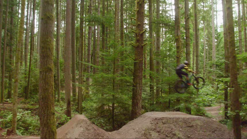A person using a dirt ramp in the forest to do tricks on his mountain bike
