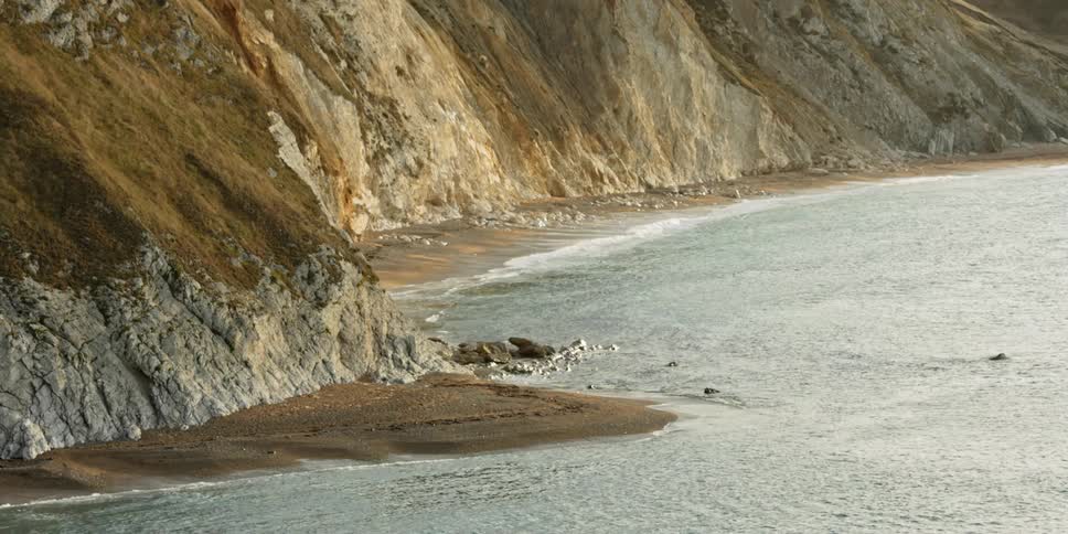 Water laps the shoreline next to a steep rock face