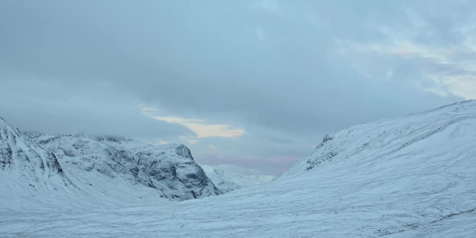 Snow blankets a mountain range under a cloudy sky