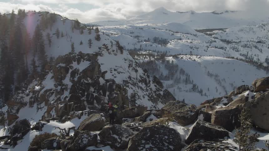 Two people hike across snow covered mountain carrying skis