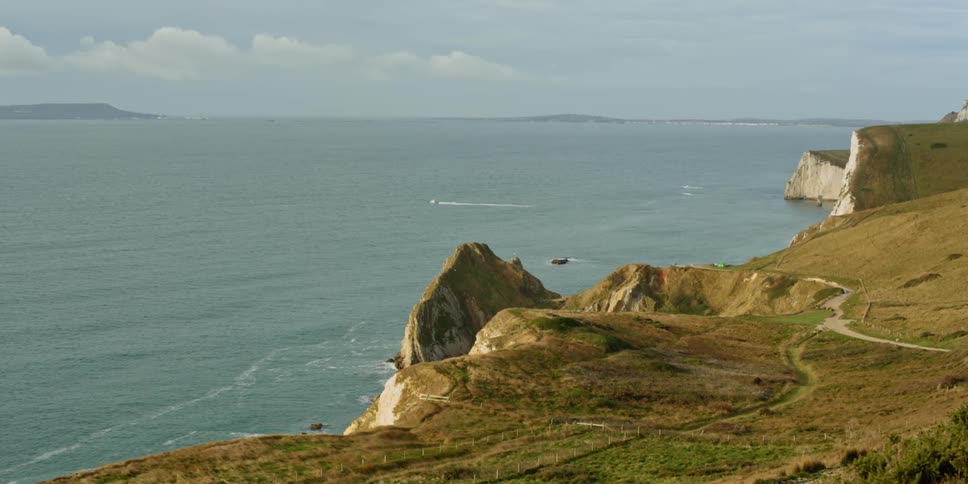 Grass covers the plains that give way to rocky cliffs that rise up above the ocean along a beautiful coastline