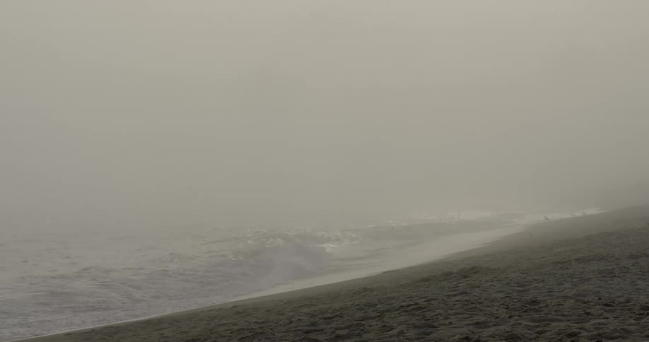 Waves lap a beach on a hazy morning