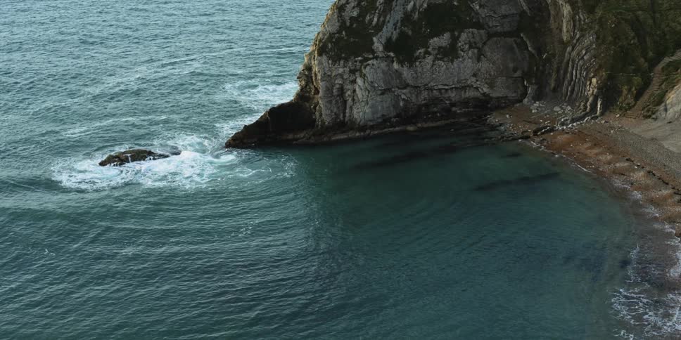 Ocean waves crash onto a cliff and beach shoreline