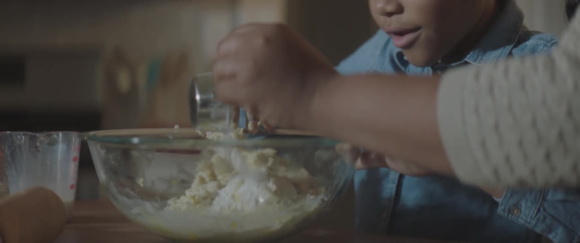 A woman and her daughter are mixing ingredients in a glass mixing bowl