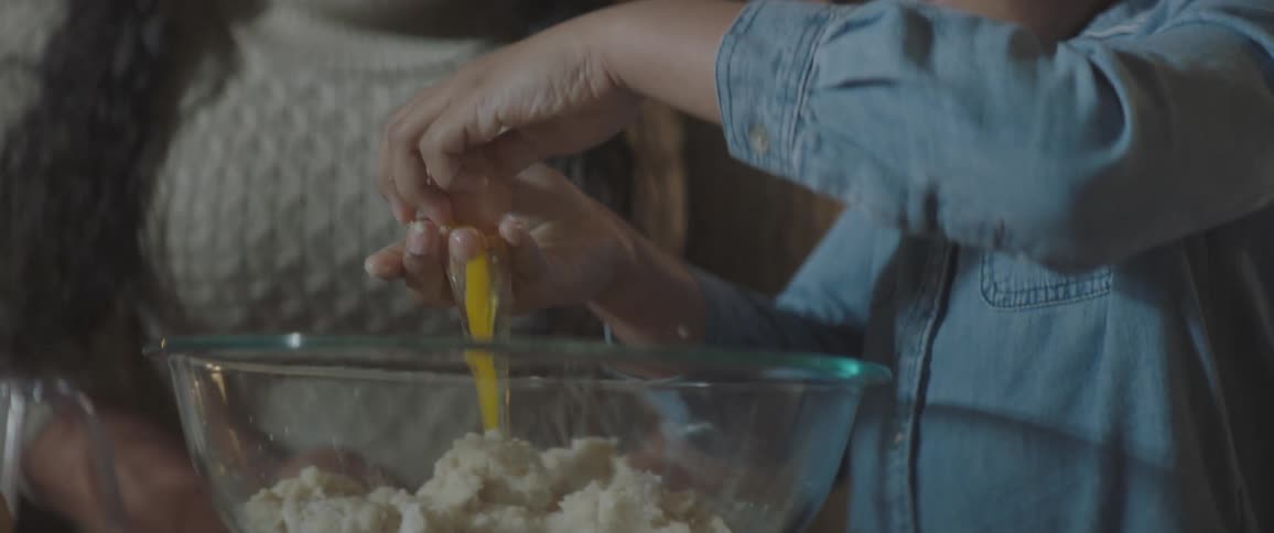 Mother teaching daughter how to break eggs