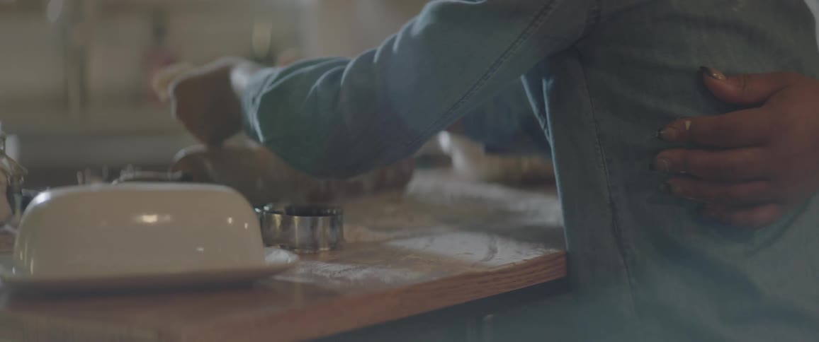 One person has their arm around another while they using a rolling pin flour and dough