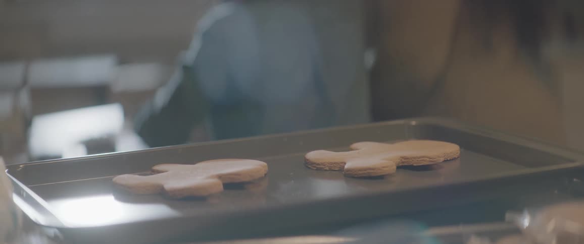 Gingerbread men are sitting on a cookie sheet behind a woman and young girl