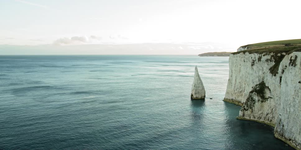 Calm ocean waters roll against white chalk cliffs in daylight