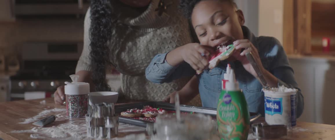 Mother watching her daughter take a bite of a decorated christmas cookie