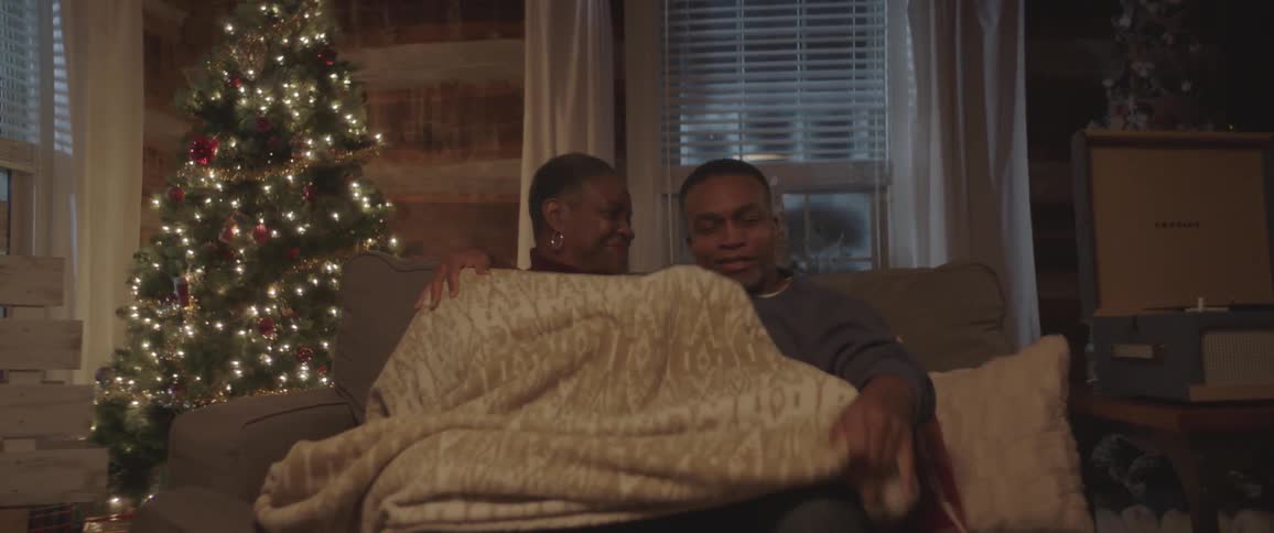 A man and woman cover up with a blanket and cuddle on the couch