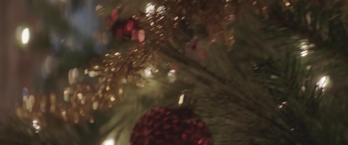 A tree is adorned with a gold garland white lights and ball ornaments