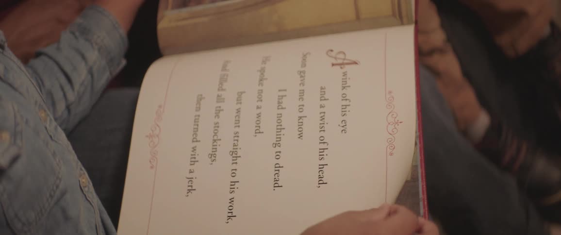 A child sitting next to his mom turns the pages of a book that lays across their laps