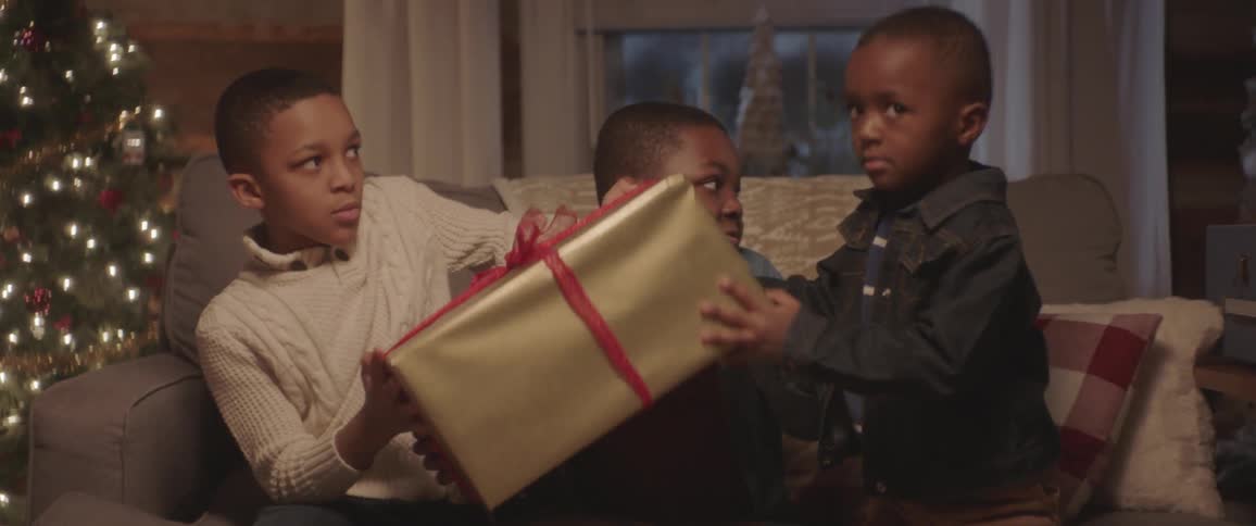 Three children are sitting on a couch shaking a wrapped present