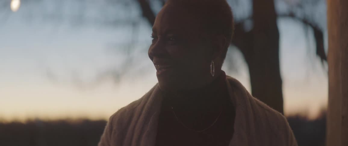 Senior black woman holds a tray of cookies and marshmallow outdoors at dusk