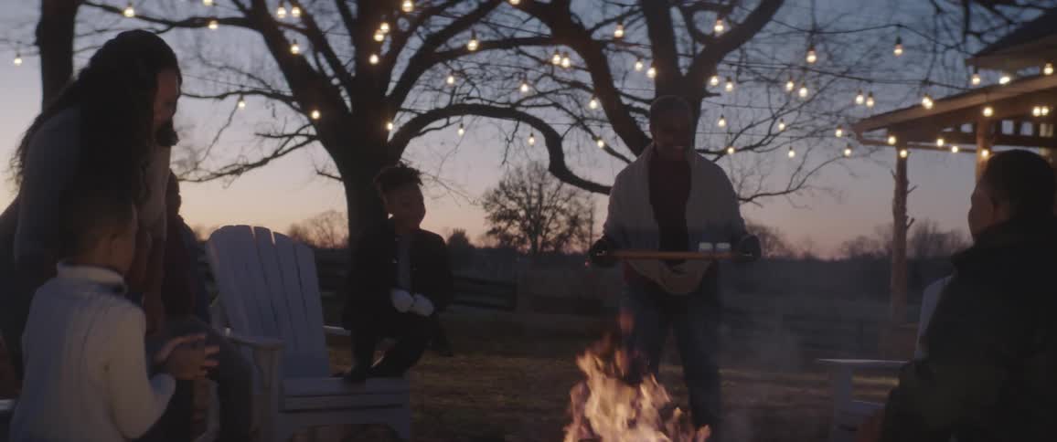 A grandmother brings a plate of marshmallows out to a fire to make smores