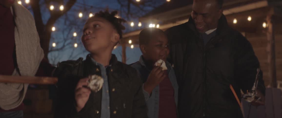 A young girl and boy are eating roasted marshmallows near a fire with their parents