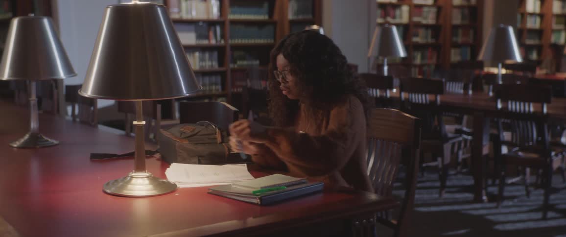Black curly hair woman sits at the table in the library